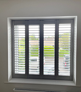 an open black bifold shutter on a window looking out to a car park