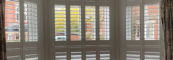 bay shutters in two tiers installed on a bay window with curtains to the sides