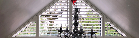 a triangular shaped shutter installed onto a window with a chandelier hanging in front 
