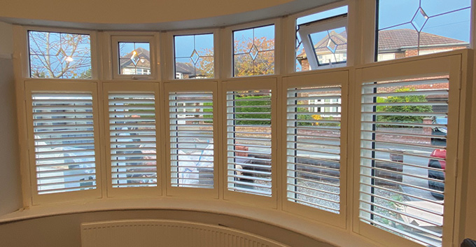 curved bay shutters installed onto a window with uncovered windows above