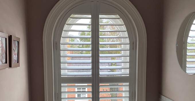 a shaped shutter shamed for an arched window in a bathroom