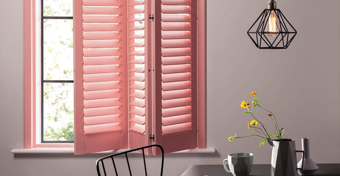 a pink bifold shutter installed in a room with a table with a jug of flowers
